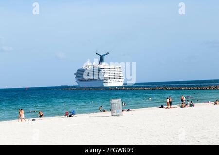 Miami, USA - 18 agosto 2014: Persone che si godono la spiaggia accanto alla nave da crociera vittoria di Carnevale lasciando Miami porto per i Caraibi. Foto Stock