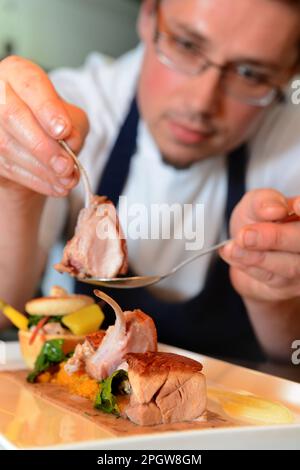 Il capo chef Kuba Winkowski assembla il piatto maiale arrosto con la carota Quinoa al Nest con piume nell'Oxfordshire. Foto Stock