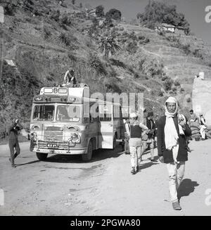 1950s, storico, collina in Nepal, su una strada di montagna polverosa, un autobus di trasporto pubblico, passeggeri fuori, un uomo che sposta bagagli dal tetto. L'autobus ha due porte, in (davanti) out (dietro). Foto Stock