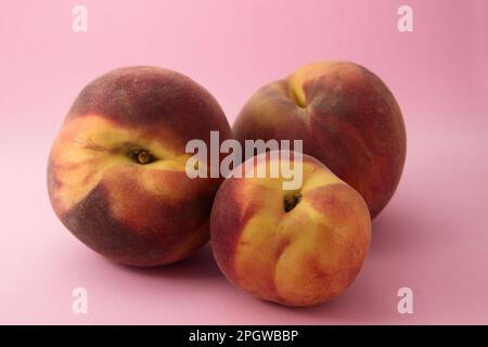 Primo piano di una vita ferma di tre pesche mature di diverse dimensioni su sfondo rosa Foto Stock