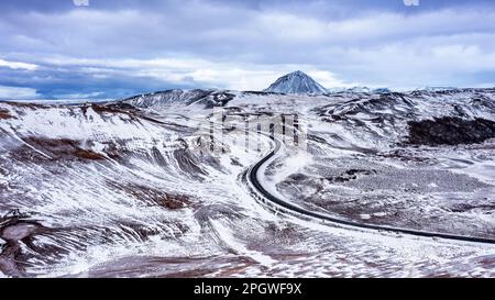 Vista aerea di una strada attraverso l'area geotermica di Hverir nel nord dell'Islanda, con il Monte Namafjall sullo sfondo. Neve coperto scena invernale. Foto Stock