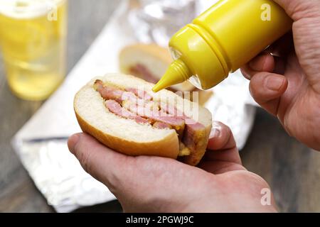 Mettere la senape su un panino di pancetta di Peameal. Il piatto di Toronto Foto Stock