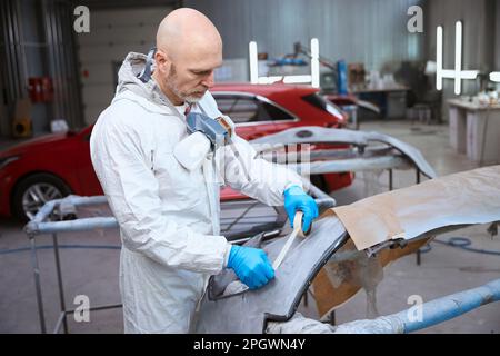 L'addetto alla riparazione auto prepara il paraurti dell'auto per la verniciatura Foto Stock