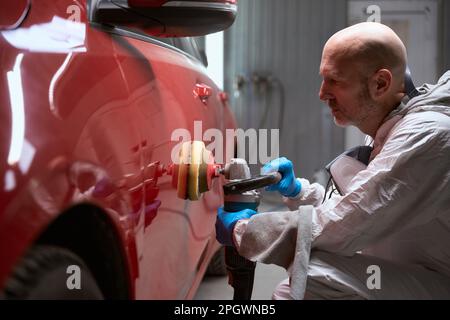 L'uomo lucida il corpo dell'automobile rossa dopo la raddrizzatura e la verniciatura Foto Stock