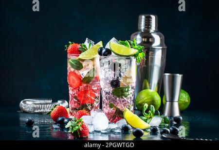 Cocktail Mojito di fragole e mirtilli con lime, rum bianco, soda, zucchero di canna, menta, e ghiaccio in vetro highball su fondo blu profondo. Estate Foto Stock