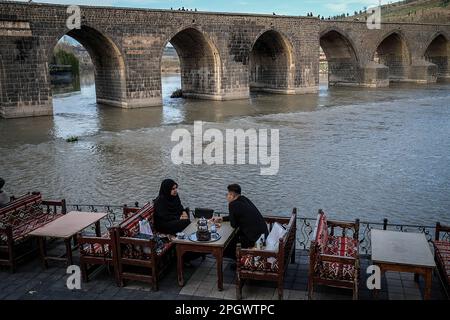 Diyarbakir, Turchia. 22nd Mar, 2023. La gente si è vista seduta in un Cafè accanto al ponte. Il ponte Tigris, conosciuto come il ponte con dieci occhi, è uno dei ponti più antichi costruiti sul fiume Tigri. È noto che il ponte fu costruito dai Marwanidi nel 1065. (Foto di Murat Kocabas/SOPA Images/Sipa USA) Credit: Sipa USA/Alamy Live News Foto Stock