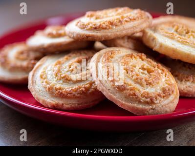 Biscotti a spirale di zucchero su piatto rosso su tavolo di legno, primo piano. Biscotti dolci fatti in casa. Concetto di pasticceria Foto Stock