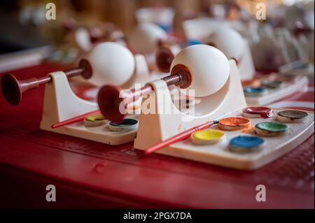 Uova di Pasqua bianche fai da te con strumenti di pittura acquerello su tavolo rosso. Decorazione fatta a mano con uova di Pasqua. Foto Stock