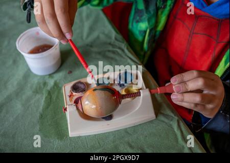 Uova di Pasqua bianche fai da te con strumenti di pittura acquerello su tavolo rosso. Uova di Pasqua decoratimg a mano. Foto Stock