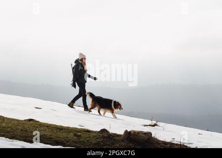 Ragazza con abiti invernali che cammina con il suo cane sulle montagne coperte di neve Foto Stock