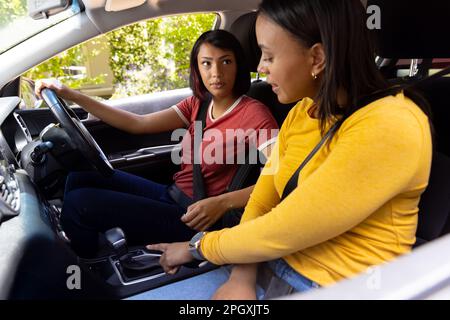 Sorelle biraciali felici seduti in auto a parlare, una sorella dando l'altra una lezione di guida Foto Stock