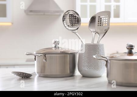 Pentole in acciaio inox e utensili da cucina su un tavolo bianco all'interno Foto Stock