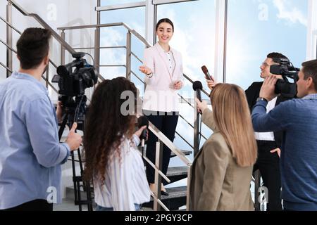 Felice donna d'affari che parla con un gruppo di giornalisti al coperto Foto Stock