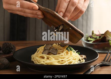 Donna affettare il tartufo su spaghetti a tavola di legno, primo piano Foto Stock