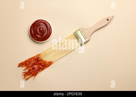 Pittura a pennello con spaghetti immersi in ketchup su fondo beige, giacitura piatta. Concetto creativo Foto Stock