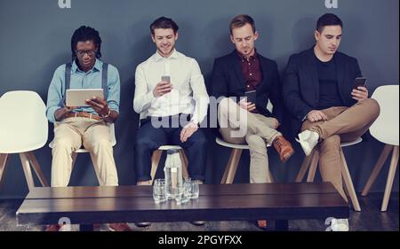 Ottenere i suggerimenti dell'ultimo minuto per l'intervista. un gruppo di uomini d'affari che utilizzano dispositivi wireless diversi in attesa di un colloquio. Foto Stock