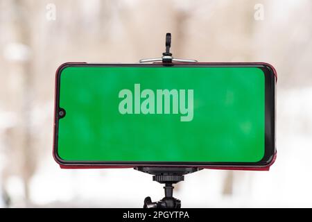 un telefono cellulare con schermo verde si trova su un supporto flessibile sulla strada all'aperto in inverno Foto Stock