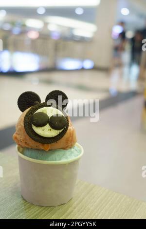 Una tazza di gelato con la guarnizione di biscotto simile al topo servita sul tavolo di legno con fondo sfocato. Foto Stock