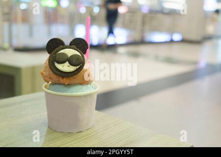 Una tazza di gelato con la guarnizione di biscotto simile al topo servita sul tavolo di legno con fondo sfocato. Foto Stock
