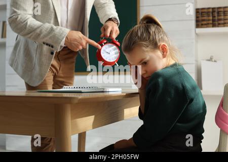 Insegnante con sveglia scogliendo allievo per essere in tarda classe Foto Stock