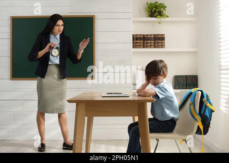 Insegnante con sveglia scogliendo allievo per essere in tarda classe Foto Stock