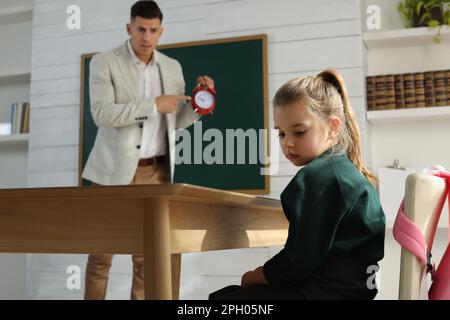 Insegnante con sveglia scogliendo allievo per essere in tarda classe Foto Stock