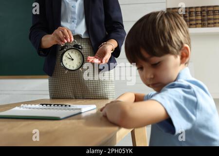 Insegnante scolding allievo per essere in ritardo in classe, concentrarsi sulla sveglia Foto Stock