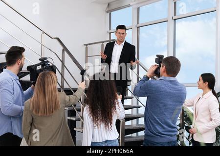 Buon uomo d'affari che parla con un gruppo di giornalisti al coperto Foto Stock