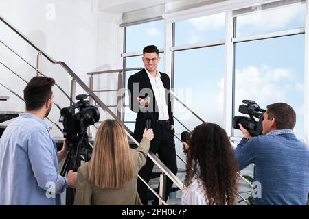 Buon uomo d'affari che parla con un gruppo di giornalisti al coperto Foto Stock