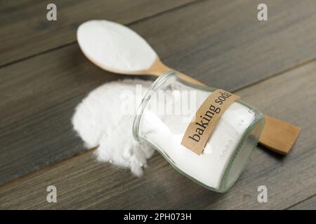 Vaso rovesciato e cucchiaio con bicarbonato su tavolo di legno, primo piano Foto Stock