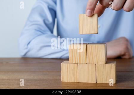 Uomo costruzione piramide di cubi su tavolo di legno, guardaroba. Spazio per il testo Foto Stock