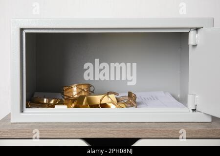 Cassaforte aperta in acciaio con barre d'oro e gioielli su tavolo di legno su sfondo bianco Foto Stock