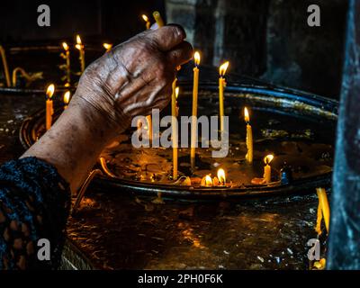 la mano della donna anziana che illumina una candela in chiesa Foto Stock