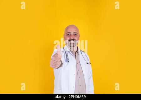 Il medico caucasico europeo di mezza età si alza. Terapista allegro in cappotto bianco, medicina di consiglio. Sfondo giallo isolato, spazio copia. Foto Stock