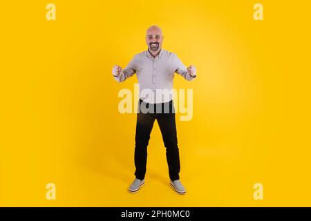 L'intera lunghezza del corpo ha lasciato l'uomo di mezza età che fa il gesto del vincitore. Calvo uomo del ventre caucasico con camicia. Il Padre celebra il concetto. Foto Stock