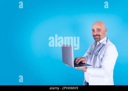 Medico caucasico che usa il computer portatile. Isolato sfondo blu studio, spazio copia. Idea di concetto di servizio di consultazione online. Uomo medico in cerca. Foto Stock