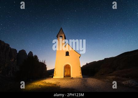 Incredibile vista sulla piccola cappella iIlluminata - Kapelle Ciapela sul Passo Gardena, Dolomiti italiane. Stelle scintillanti nel cielo scuro di notte sullo sfondo. Dolomiti, Italia. Fotografia di paesaggi Foto Stock