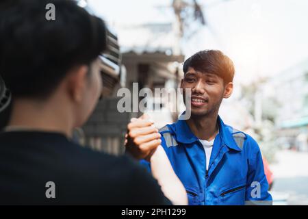 Cliente giovane uomo che scuote le mani con meccanico auto in uniforme rossa avendo un affare al servizio di auto Foto Stock