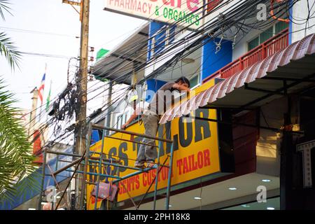 Un installatore in Thailandia in piedi su impalcature installa un cartello sulla facciata di un edificio. Thailandia, Krabi - 10.12.2022 Foto Stock