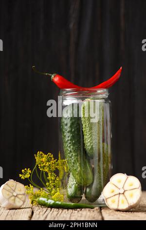 Cetrioli freschi in un vaso di vetro per la casa inscatolamento, peperoncini, aneto, aglio su un vecchio sfondo di legno. Cetrioli e spezie per marinata fatta in casa. Foto Stock