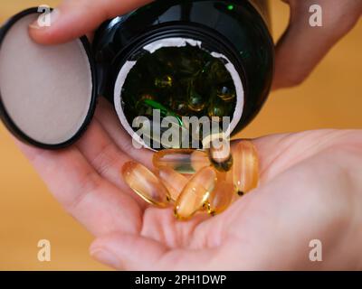 Donna versando le capsule di softgel di vitamina fuori da un vaso alla sua mano Foto Stock