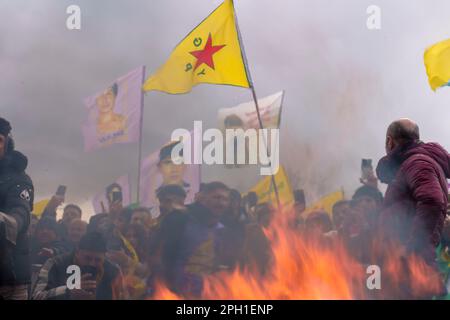 25 marzo 2023, Assia, Francoforte sul meno: I partecipanti si alzano con le bandiere davanti a un incendio. Alla celebrazione centrale del nuovo anno curdo 'Newroz'. Al centro è una bandiera del YPG, una milizia curda armata. Migliaia di persone provenienti da tutta la Germania si sono riunite a Rebstockpark per celebrare il nuovo anno curdo 'Newroz'. Foto: Andreas Arnold/dpa Foto Stock