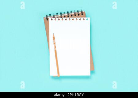 Taccuino con matita. Quaderno scolastico su sfondo blu chiaro, blocco note a spirale sul tavolo. Vista dall'alto del notebook aperto con pagine vuote, blocco note per ufficio fl Foto Stock