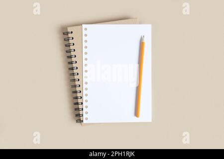 Notebook con matita. Quaderno scuola su sfondo beige neutro, quaderno a spirale sul tavolo. Vista dall'alto del notebook aperto con pagine vuote, blocco note per ufficio Foto Stock