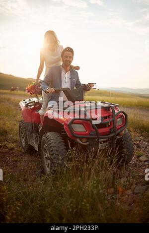 Amabili sposi novelli che guidano quad insieme nella natura; concetto di matrimonio rurale Foto Stock
