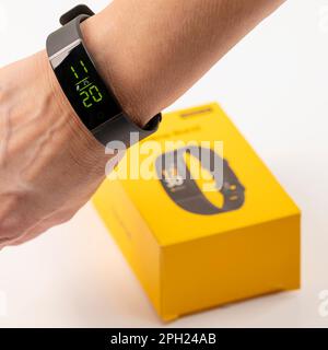 Una donna mostra un nuovissimo smartwatch Realme Band 1 con ampio display a colori e Fitness Tracker al polso, con il box sullo sfondo Foto Stock