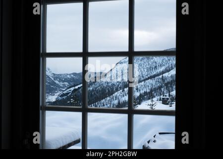 Vista dalla finestra dall'accogliente cabina in legno alle montagne innevate durante l'inverno. Foto Stock