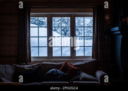 Vista dalla finestra dall'accogliente cabina in legno alle montagne innevate durante l'inverno. Foto Stock