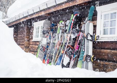 Hemsedal, Norvegia - 13 marzo 2023: Sci di montagna e snowboard in piedi su una parete di cabina di legno durante la nevicata. Foto Stock