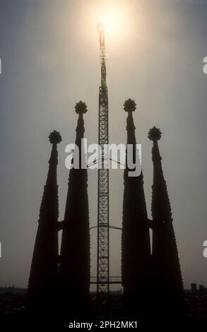 1991 immagine dell'archivio della silhouette dei lavori di costruzione della Sagrada Familia a Barcellona. Mostra le torri della chiesa con una gru a torre che si stagliano contro il sole. Foto Stock